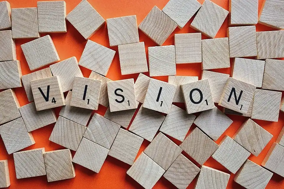 Square wooden letter tiles scattered on an orange surface, six of them spelling the word VISION