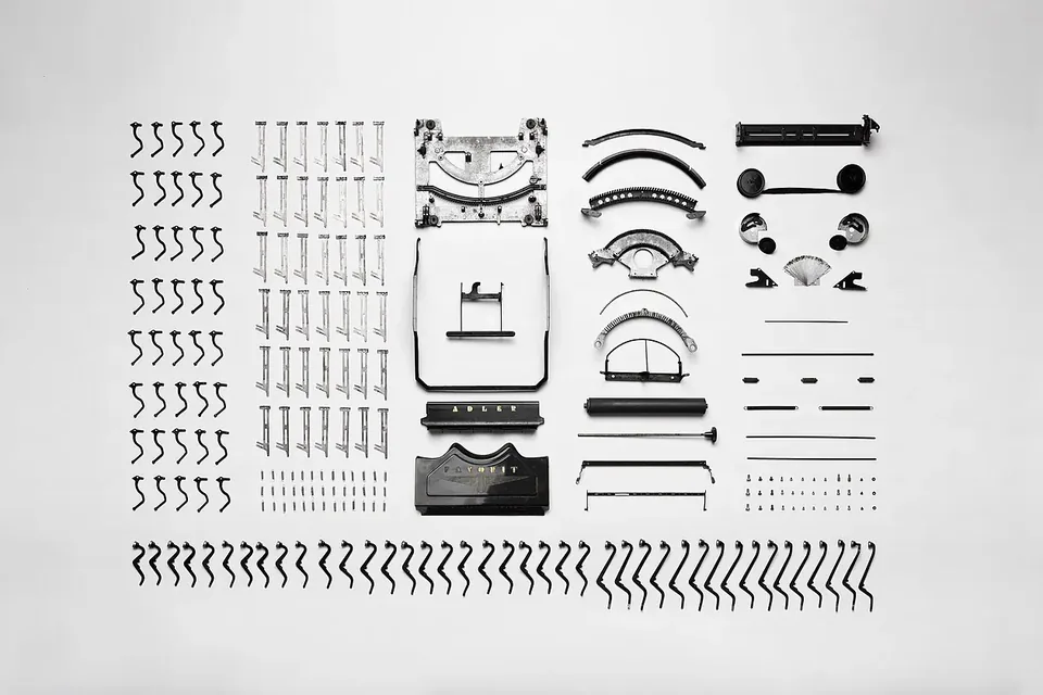 The parts of a dismantled mechanical typewriter laid out in neat rows on a white background