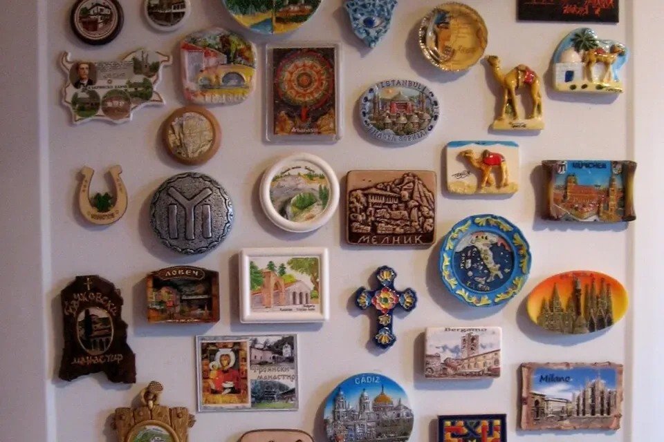 A white fridge door covered in colourful souvenir magnets from many towns
